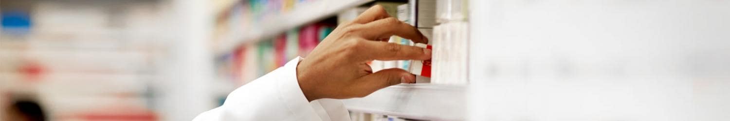 白衣を着た人が薬局の棚にある箱に手を伸ばしています。