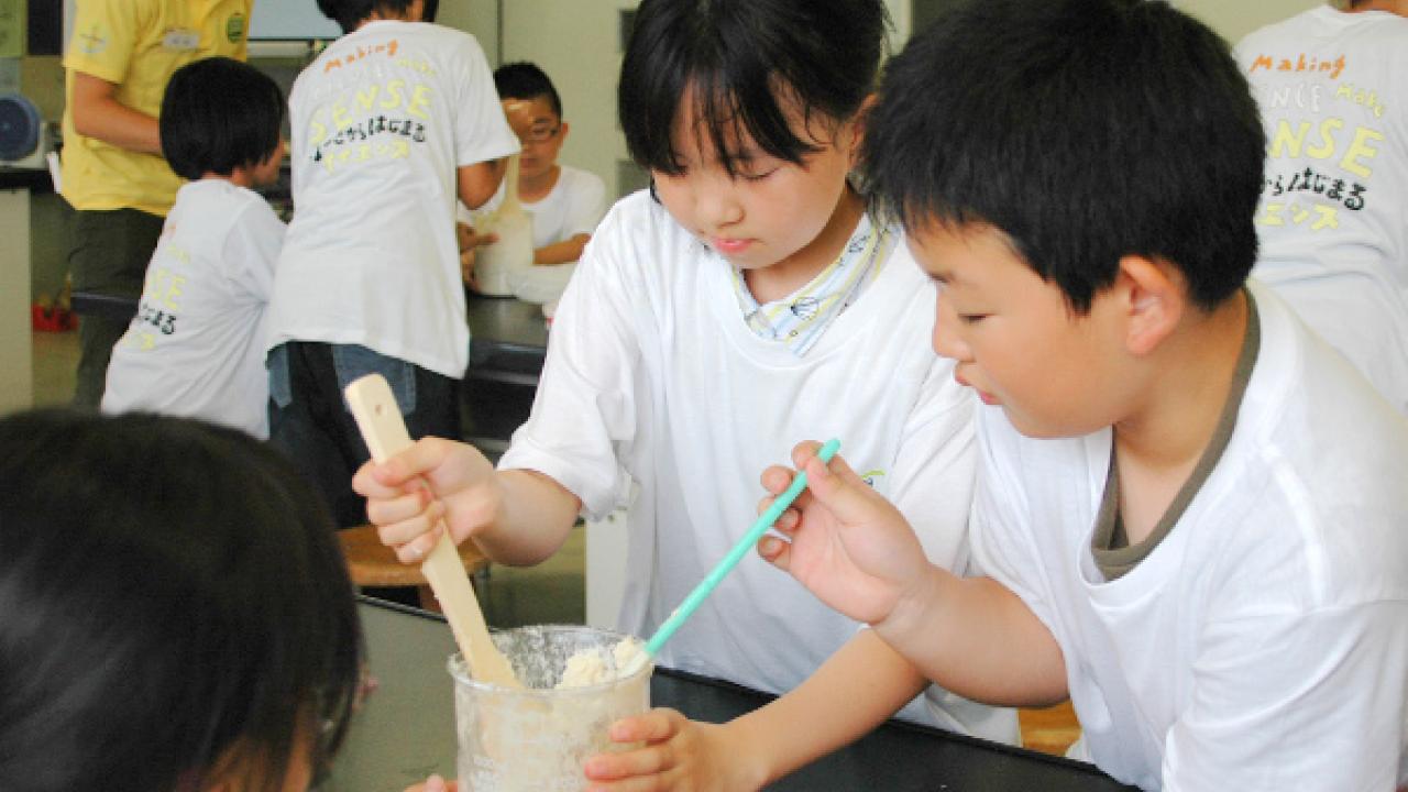 教室の子どもたちは、木製とプラスチック製のヘラを使ってボウルの中の材料を混ぜるグループ活動を行っています。