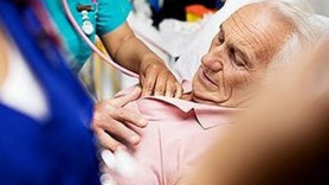 医療従事者が病院のベッドに横たわる高齢男性の心拍をチェックしている。