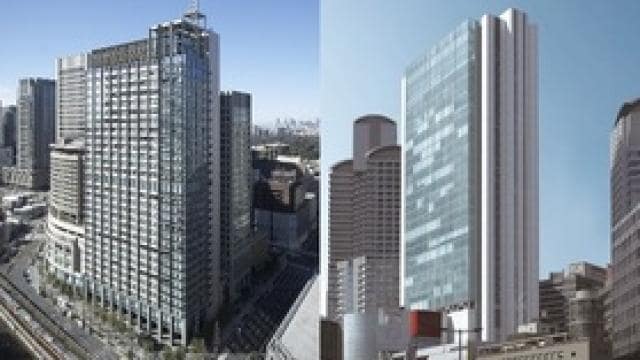 ガラス張りの高層オフィスビル 2 棟が、澄んだ空を背景に、都市部のその他の建物に囲まれて立っています。